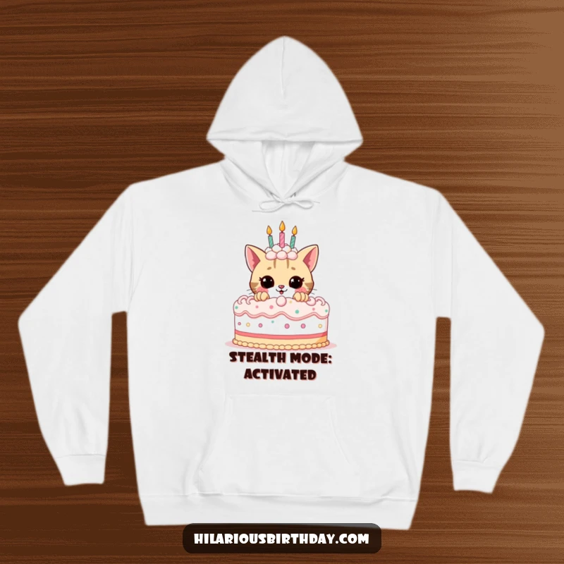 Funny birthday hoodie featuring a cute, playful cat peeking out from behind a massive, elaborately decorated birthday cake, full of mirth.