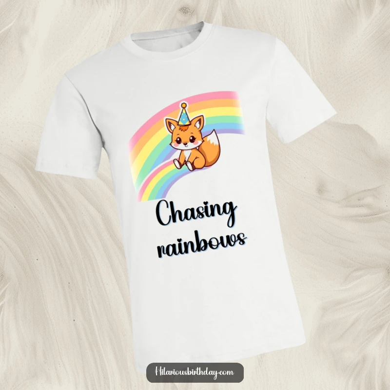 Funny t-shirt with a kawaii fox character sliding down a rainbow wearing a party crown, depicting pure joy and magical adventure.