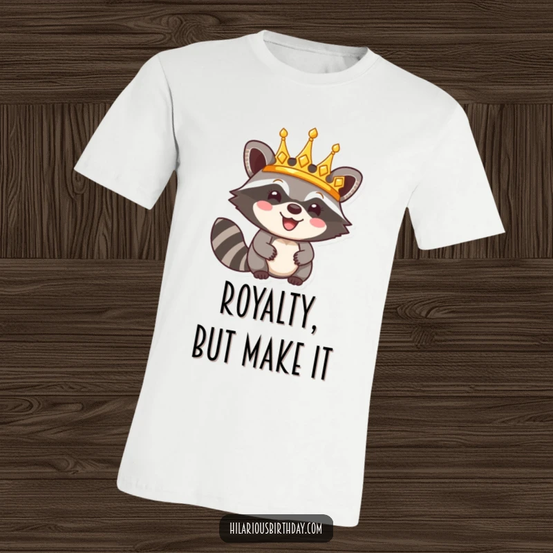 Funny t-shirt featuring a happy raccoon character triumphantly wearing a shiny golden crown, symbolizing playful dominance.